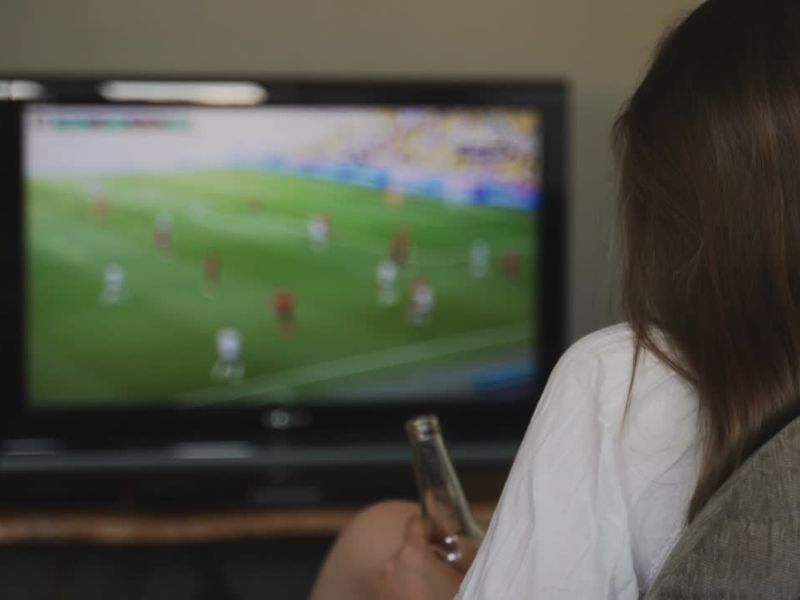devojka gleda fudbal na televizoru i pije pivo