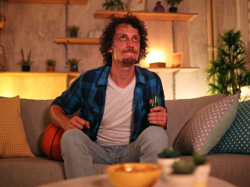 momak gleda košarku preko tv- a i drži pivo u ruci